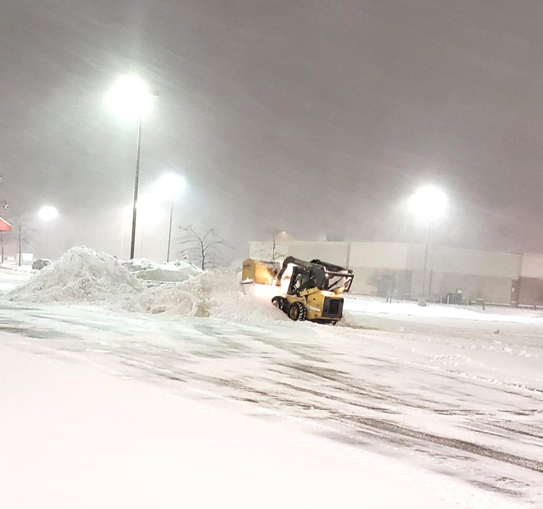 Skid steer plowing a commercial parking lot during a snowstorm